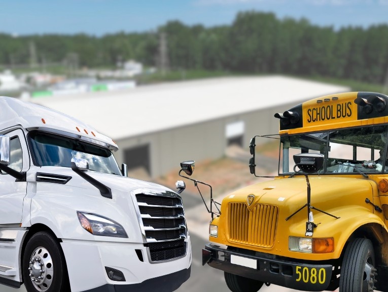 A white semi-truck and a yellow school bus parked side by side outdoors near an industrial building, representing Class A and Class B commercial driving vehicles.