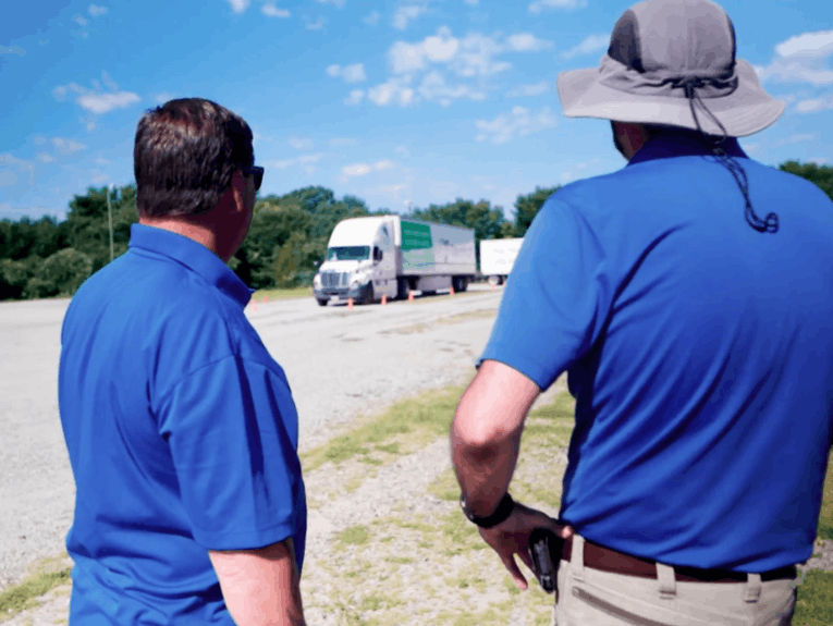 Two recruiters standing with their backs facing camera, looking forward at TransTech semi trucks