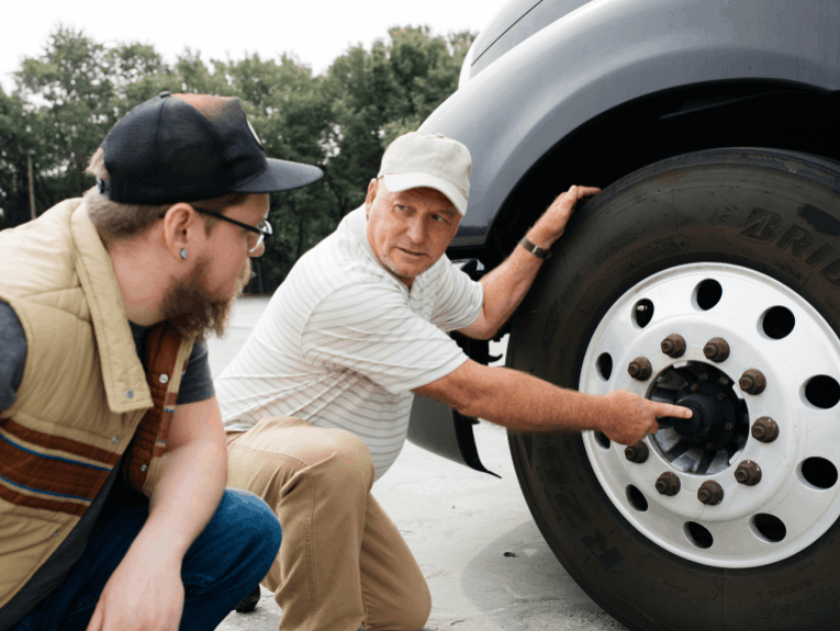 Instructor pointing at semi truck wheel. Student looking at the wheel.