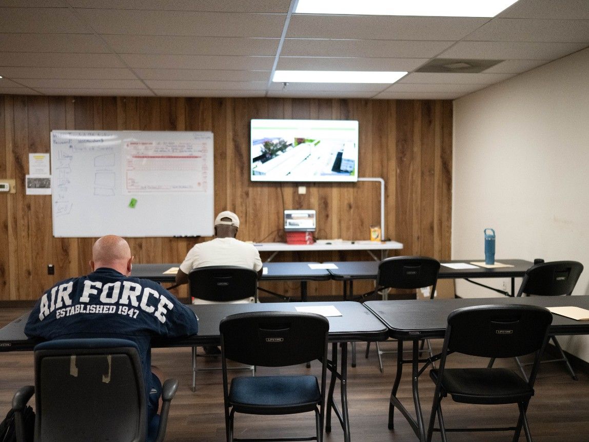 Charleston classroom with a whiteboard and TV on the wall. Three students sitting at desks.