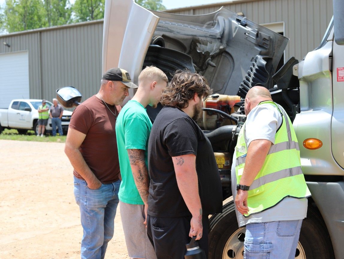 CDL instructor teaching students pre-trip inspection requirements on a semi-truck engine