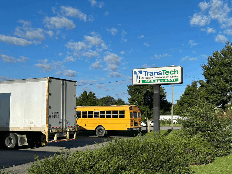 TransTech Charlotte campus sign with a bus and semi truck trailer parked in front