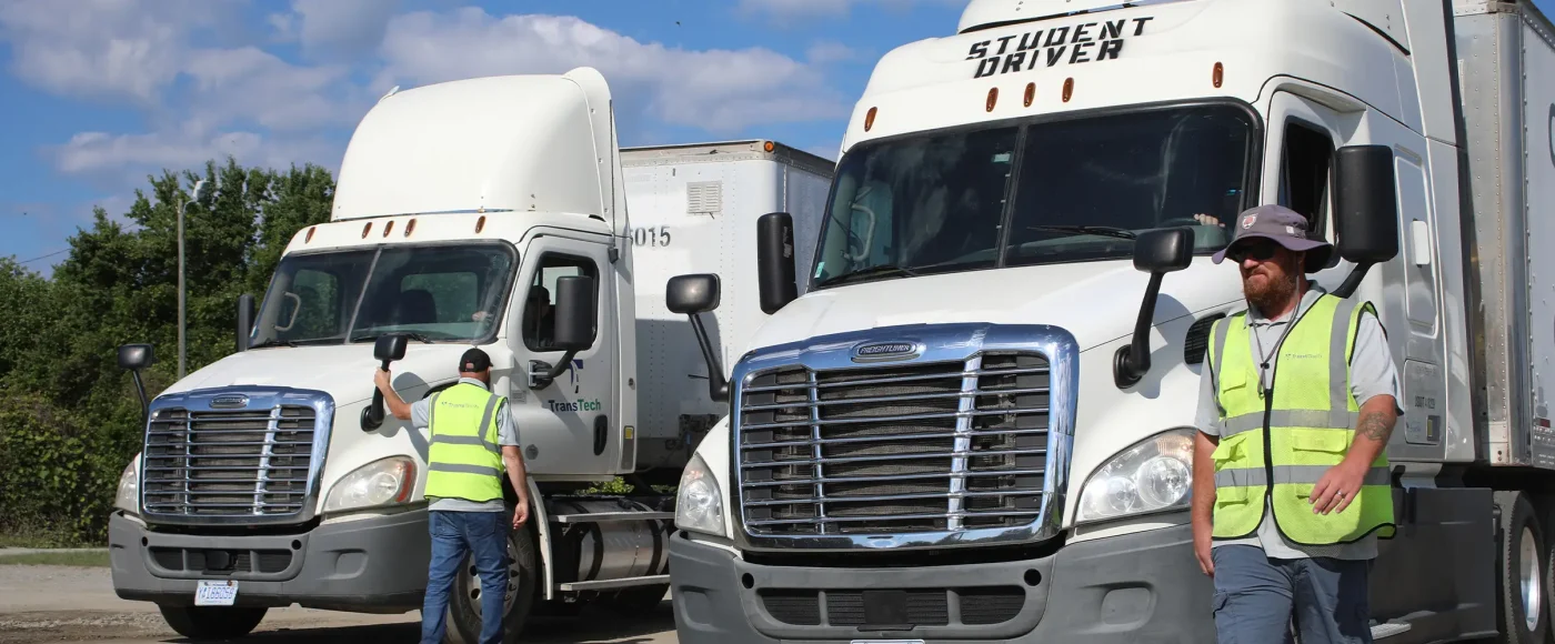 Two semi trucks driving in training yard with instructors leading them