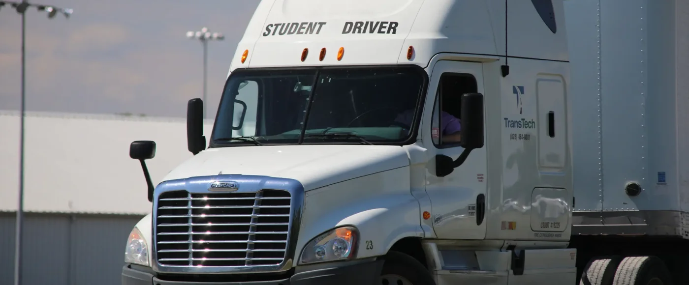 A TransTech student driver sits behind the wheel of a semi-truck, visible through the windshield as they practice maneuvering the cab
