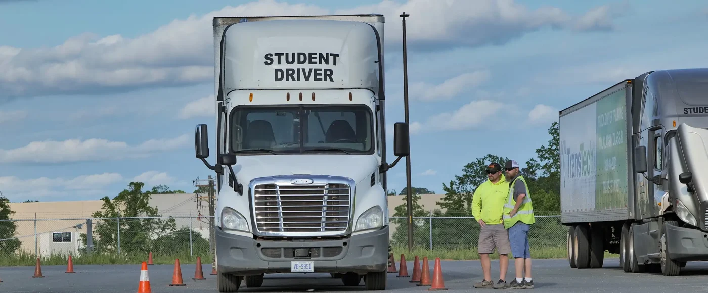 Front view of TransTech semi truck in training yard with two instructors standing nearby