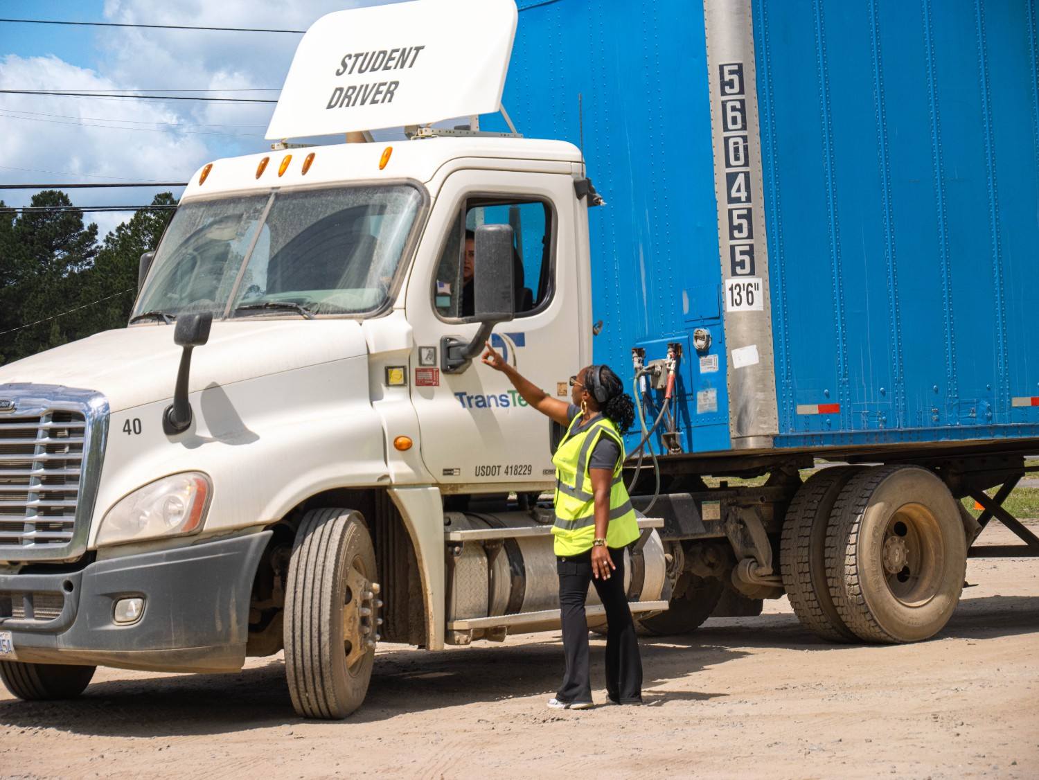 Female instructor looking up and speaking to student in semi truck cab
